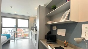 Una habitación moderna con escritorio, laptop y vista a la ciudad a través de amplias ventanas.