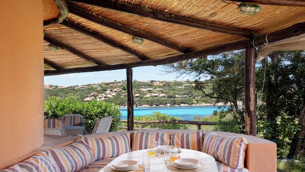 Un área de comedor al aire libre techada con una mesa dispuesta para cuatro personas, con vistas a un paisaje costero.