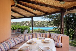 Un área de comedor al aire libre techada con una mesa dispuesta para cuatro personas, con vistas a un paisaje costero.
