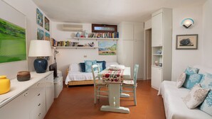 Una habitación acogedora con cama, una mesa de comedor con sillas, un sofá y un televisor. Hay estanterías y un armario pequeño.