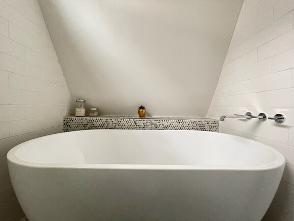 Un baño moderno con una bañera independiente, una zona de ducha con azulejos y un pequeño estante con artículos de aseo.