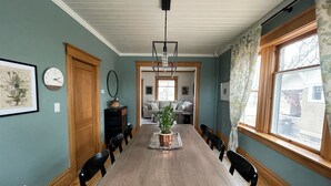 A dining room with a long wooden table, black chairs, a potted plant, and a clock on the wall. - Heron House - Elevated Vintage Downtown Victoria (Victoria)