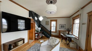 A living room with a TV, a staircase, a desk, and a patterned rug. - Heron House - Elevated Vintage Downtown Victoria (Victoria)