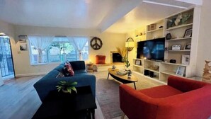 A modern living room with a sofa, a red armchair, a coffee table, and a TV. - Sea-la-Vie Retreat: Parking Included & Fire Pit (San Diego)