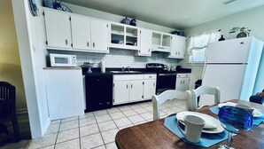 A kitchen with white cabinets, a black dishwasher, and a dining area with a wooden table and chairs.
