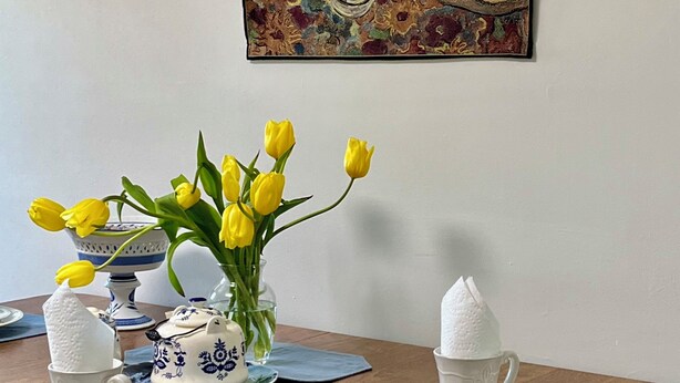 A dining table with a vase of yellow tulips, white teapots, and blue and white plates.