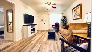 A living room with a ceiling fan, a television, a sofa, a coffee table, and a plant.