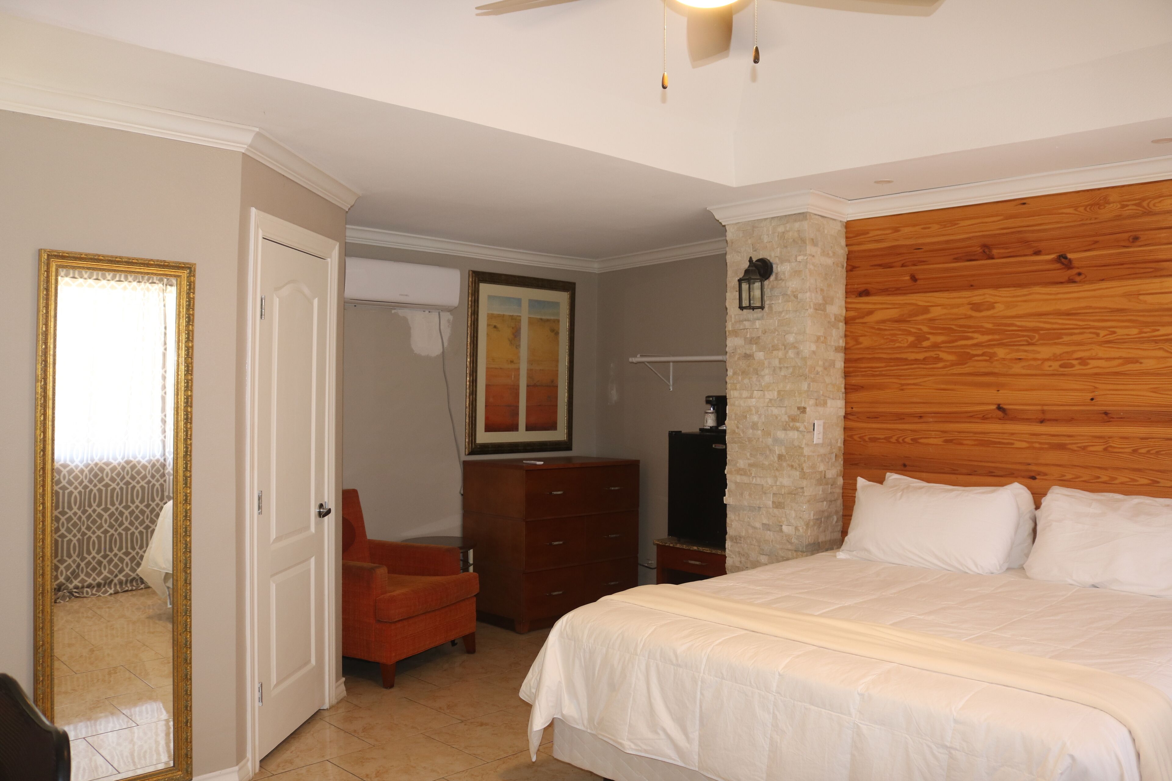 A bedroom with a large bed, a dresser, a chair, and a mirror.