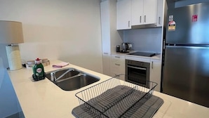 A modern kitchen with white cabinets, a stainless steel refrigerator, and a black wire dish rack on the counter. - Darwin City Retreat  2 bedrooms (Darwin City)