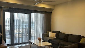A modern living room with a dark grey sofa, a white coffee table, and a large window with sheer curtains. - Darwin City Retreat  2 bedrooms (Darwin City)