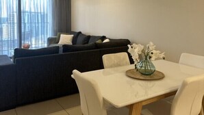 A modern living room with a dining area, a ceiling fan, and a view of the city through large windows. - Darwin City Retreat  2 bedrooms (Darwin City)