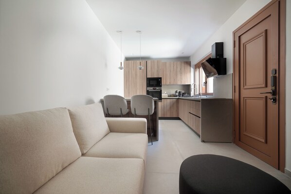 Un espacio habitable compacto con sofá, sillas, kitchenette y una puerta de madera.
