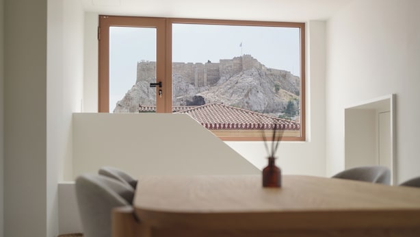 Ein Zimmer mit einem großen Fenster, das auf eine historische Mauer aus Stein und ein Ziegeldach blickt.