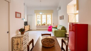 A living room with a dining table, chairs, a red refrigerator, a green sofa, and a window with a view of trees. - Casa Mameli by Wonderful Italy (Conversano)