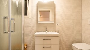 A bathroom with a white sink, mirror, and toilet, and a glass shower enclosure. - Casa Mameli by Wonderful Italy (Conversano)