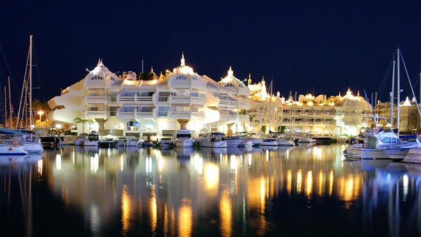 Un hotel frente al agua con varios balcones y un puerto deportivo con barcos.