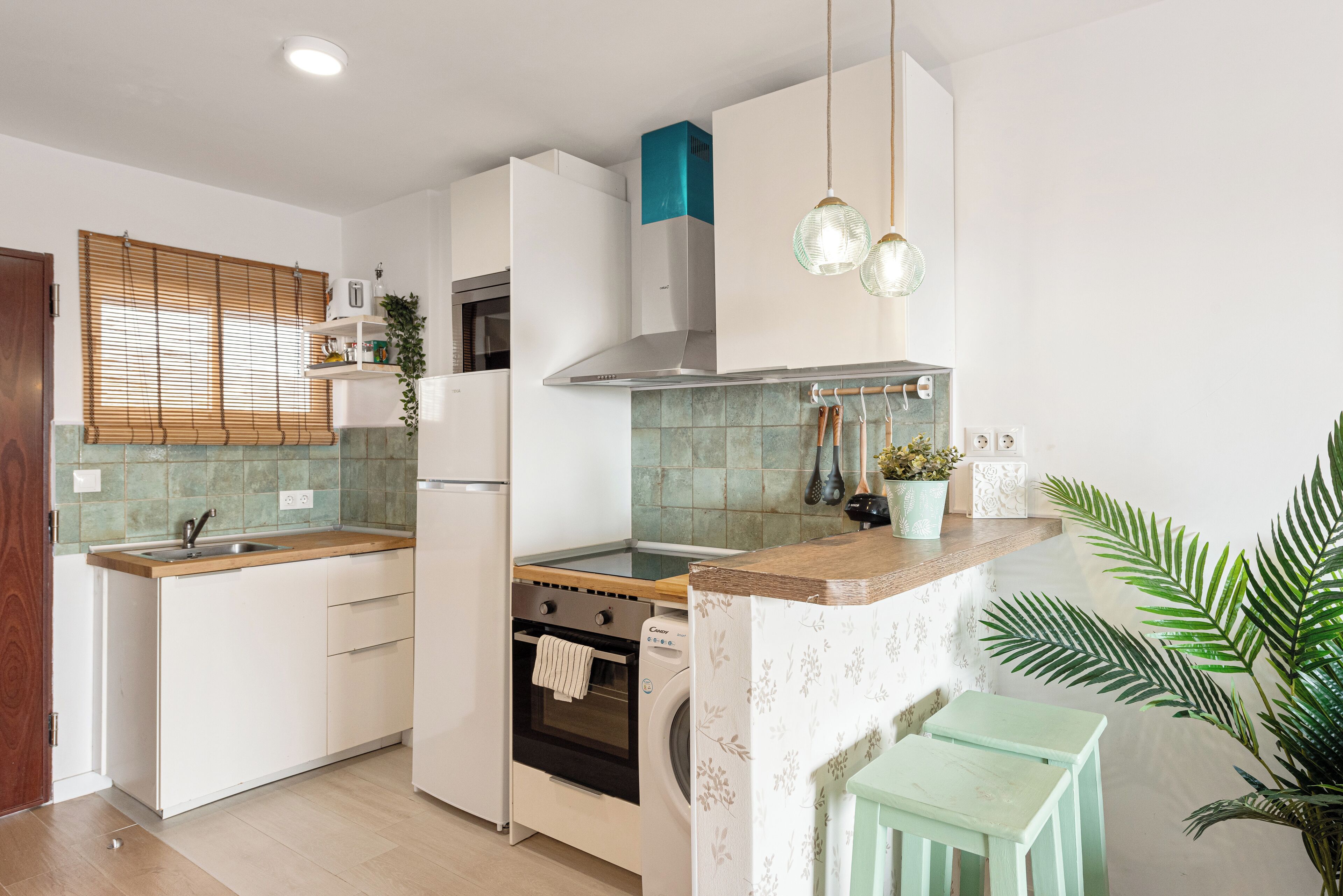 A modern kitchen with white cabinets, a wooden countertop, a built-in oven, and a washing machine.