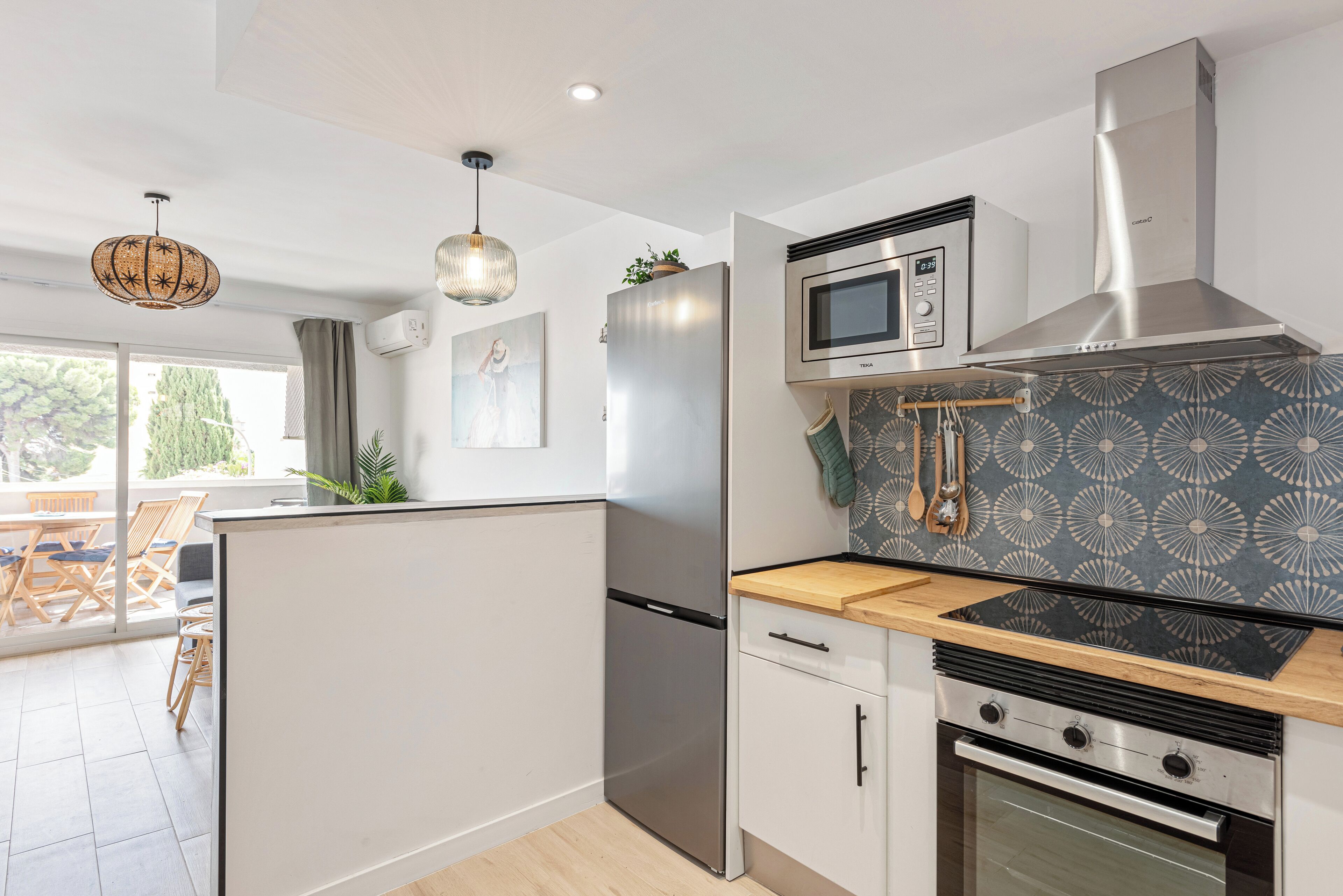 A modern kitchen with a stainless steel refrigerator, microwave, and oven. There is a wooden countertop and a patterned backsplash.