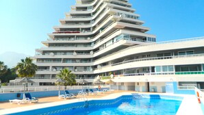 Un hotel moderno de varios pisos con piscina y tumbonas.