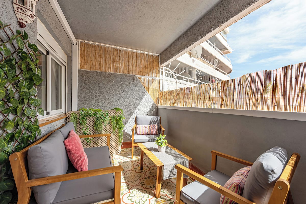 A balcony with a wooden chair, a sofa, and a small table. There is a potted plant on the table.