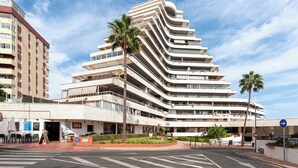 Un hotel de varios pisos con fachada curva, zona de estar al aire libre y palmeras.