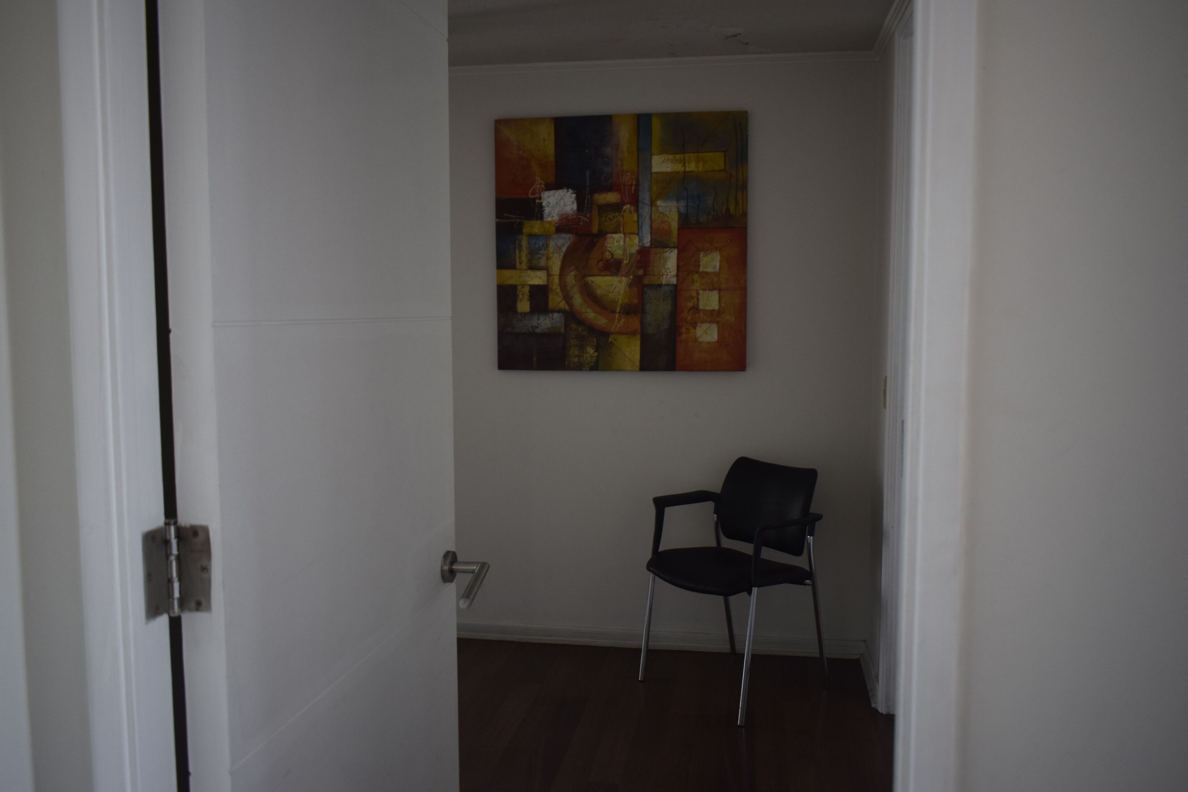A room with a door, a chair, and a wall-mounted abstract painting.