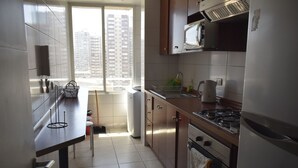 Cozinha moderna com eletrodomésticos de aço inoxidável, janela com vista para edifícios altos e piso ladrilhado.