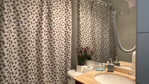 Casa de banho com cortina de chuveiro estampada com flores, uma pia com espelho e um chuveiro manual.
