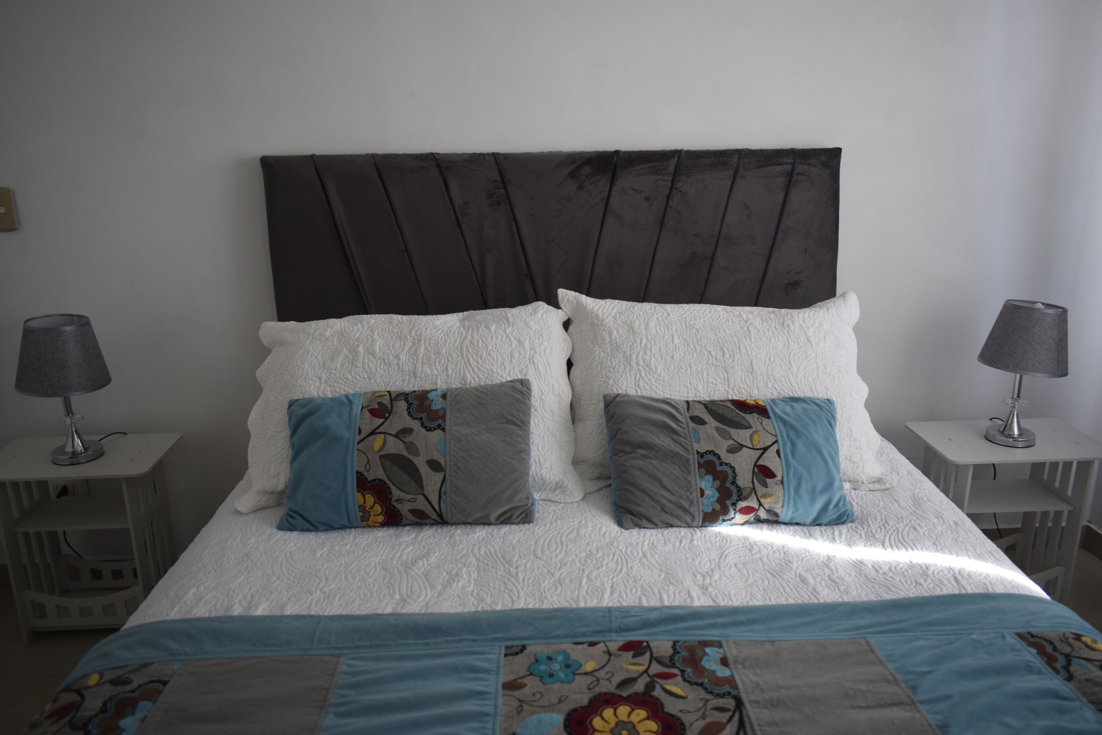 A neatly made bed with a white duvet, two pillows with floral patterns, and a blue and beige quilt.