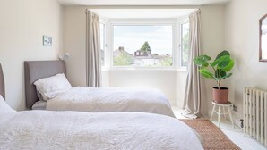 Ein Schlafzimmer mit zwei Betten, einem Fenster mit Vorhängen, einem Heizkörper und einer Topfpflanze.