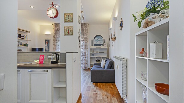 A modern kitchen with white cabinets, a coffee machine, and a dining area with a grey sofa. - Cozy Lighthouse Apartment by Wonderful Italy (Santa Margherita Ligure)