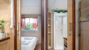 A hotel room with a bed, a window with red curtains, a shower area, and a refrigerator with magnets.