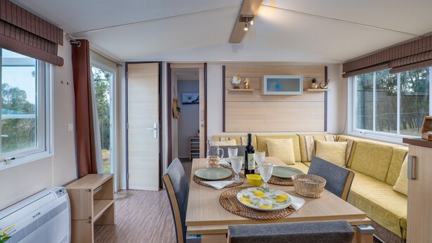 A compact, well-lit room with a dining table set for two, a sofa, and a television mounted on the wall.