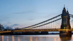 Un puente colgante con una torre central y cables, que cruza sobre una masa de agua.