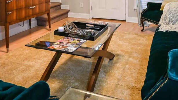 Una sala de estar con una televisión, una mesa de centro de vidrio con revistas, un sofá verde y una puerta con ventana.