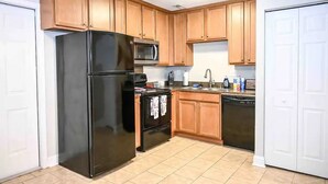 Una cocina con armarios de madera, un refrigerador negro, microondas, estufa y lavavajillas.
