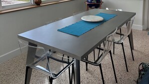 Un comedor con mesa, sillas, ventilador de techo y ventanas amplias con vista a palmeras y agua.