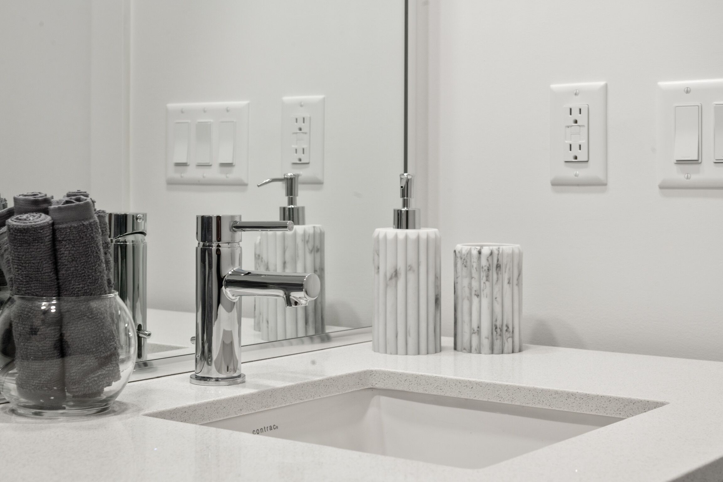 A modern bathroom with a rectangular sink, chrome fixtures, and marble-like soap dispensers.