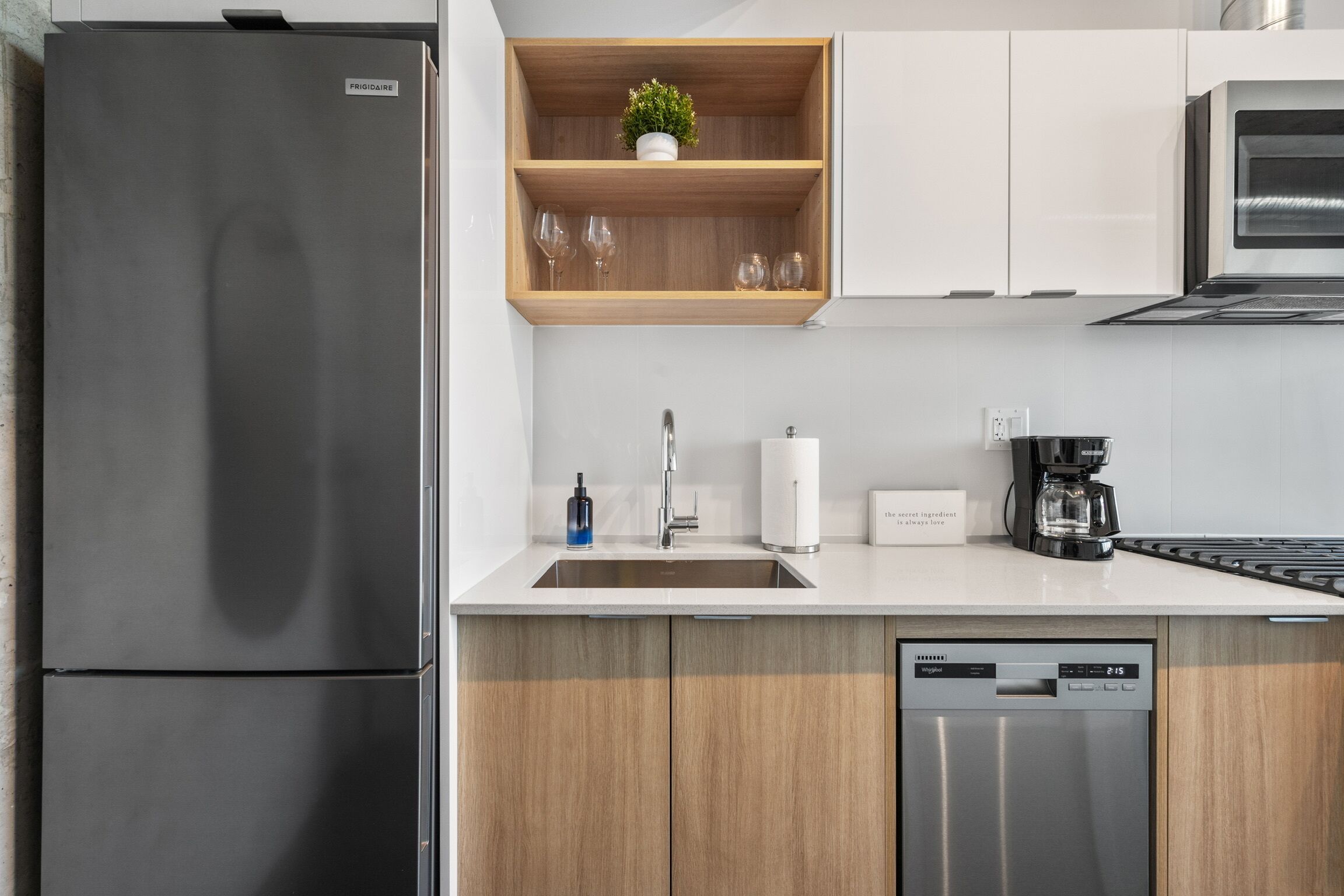 Une cuisine moderne dotée d’un réfrigérateur en acier inoxydable, de meubles en bois, d’une étagère intégrée agrémentée d’une plante, d’une machine à café et d’un lave-vaisselle.