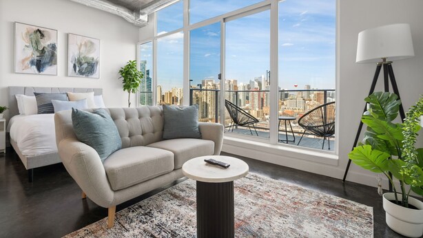 Ein modernes Wohnzimmer mit großem Fenster, einer Couch, einem Couchtisch und Blick auf die Stadt.