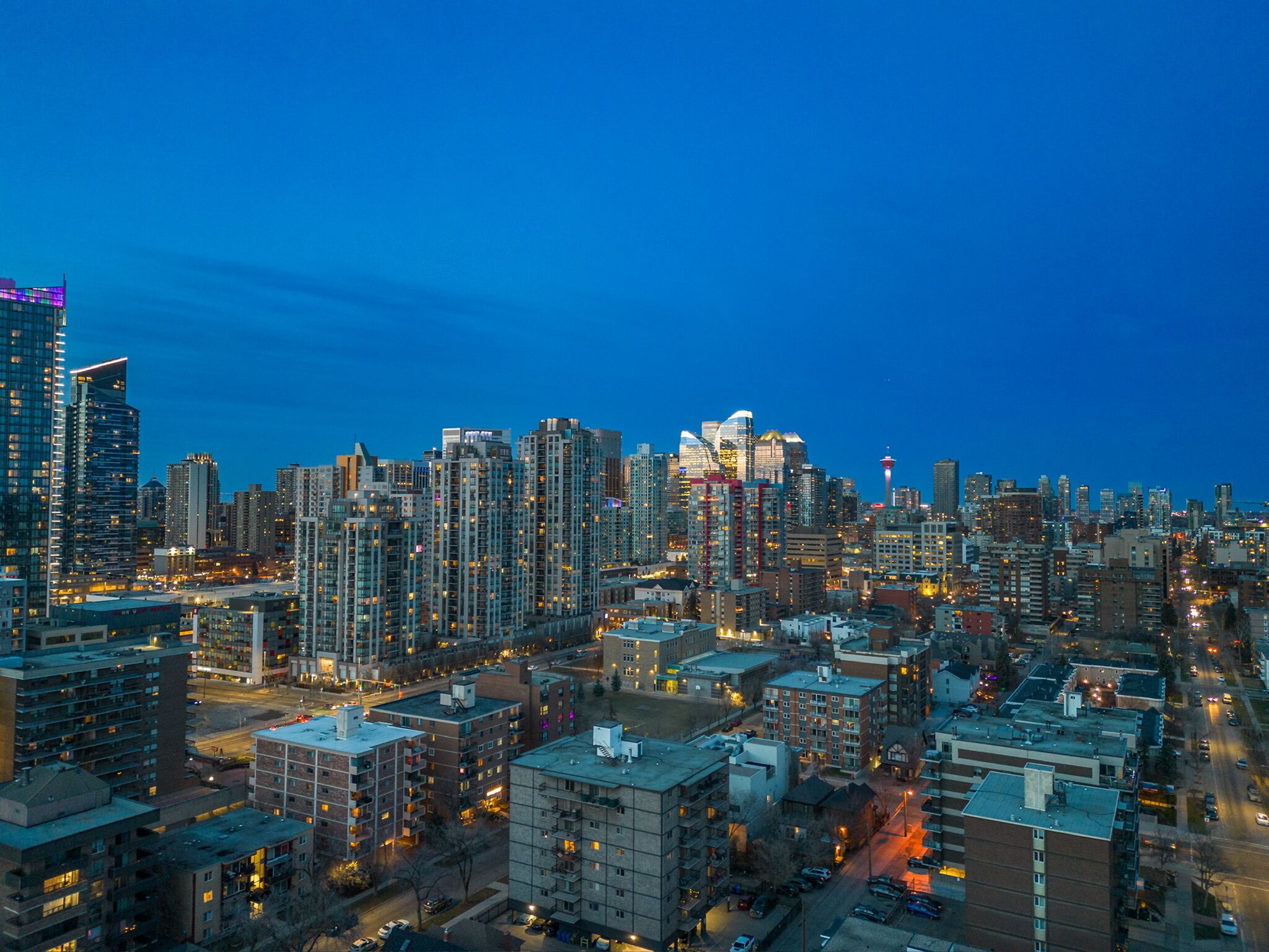 Une vue d’ensemble d’une ville au crépuscule, avec des immeubles de grande hauteur, une tour imposante et un mélange de bâtiments résidentiels et commerciaux.
