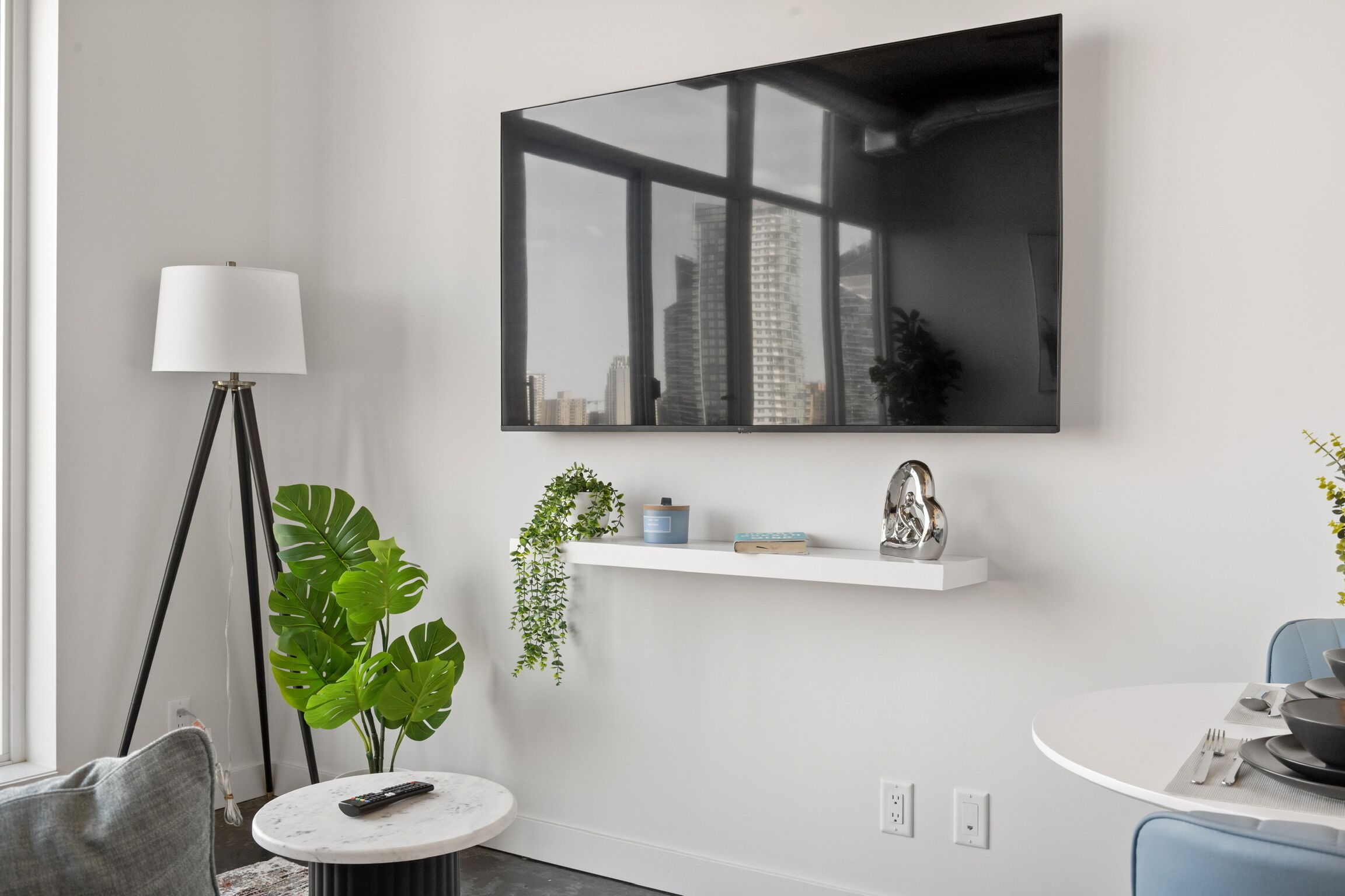 Un salon moderne avec une grande fenêtre, une table basse ronde, un lampadaire et un téléviseur fixé au mur.