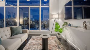 Ein modernes Wohnzimmer mit einer Couch, einem Couchtisch, einer Stehlampe und einem großen Fenster mit Blick auf die Stadt.
