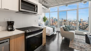 Eine moderne Küche mit Herd, Backofen und Mikrowelle, ein Bett mit Blick auf die Stadt und eine Sitzecke mit Ausblick.