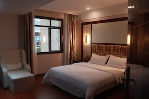 Una habitación de hotel con cama, una silla, una ventana y una lámpara fijada a la pared.