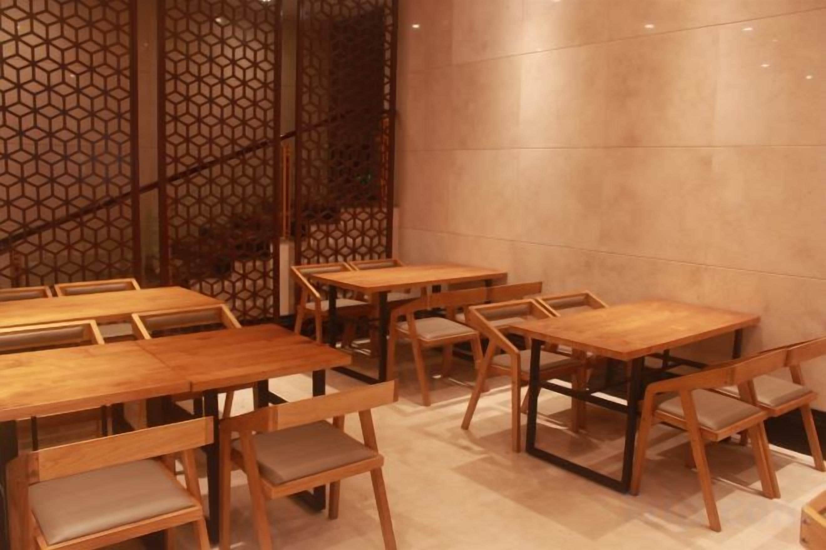 A restaurant interior with wooden tables and chairs, a decorative wall, and a tiled floor.