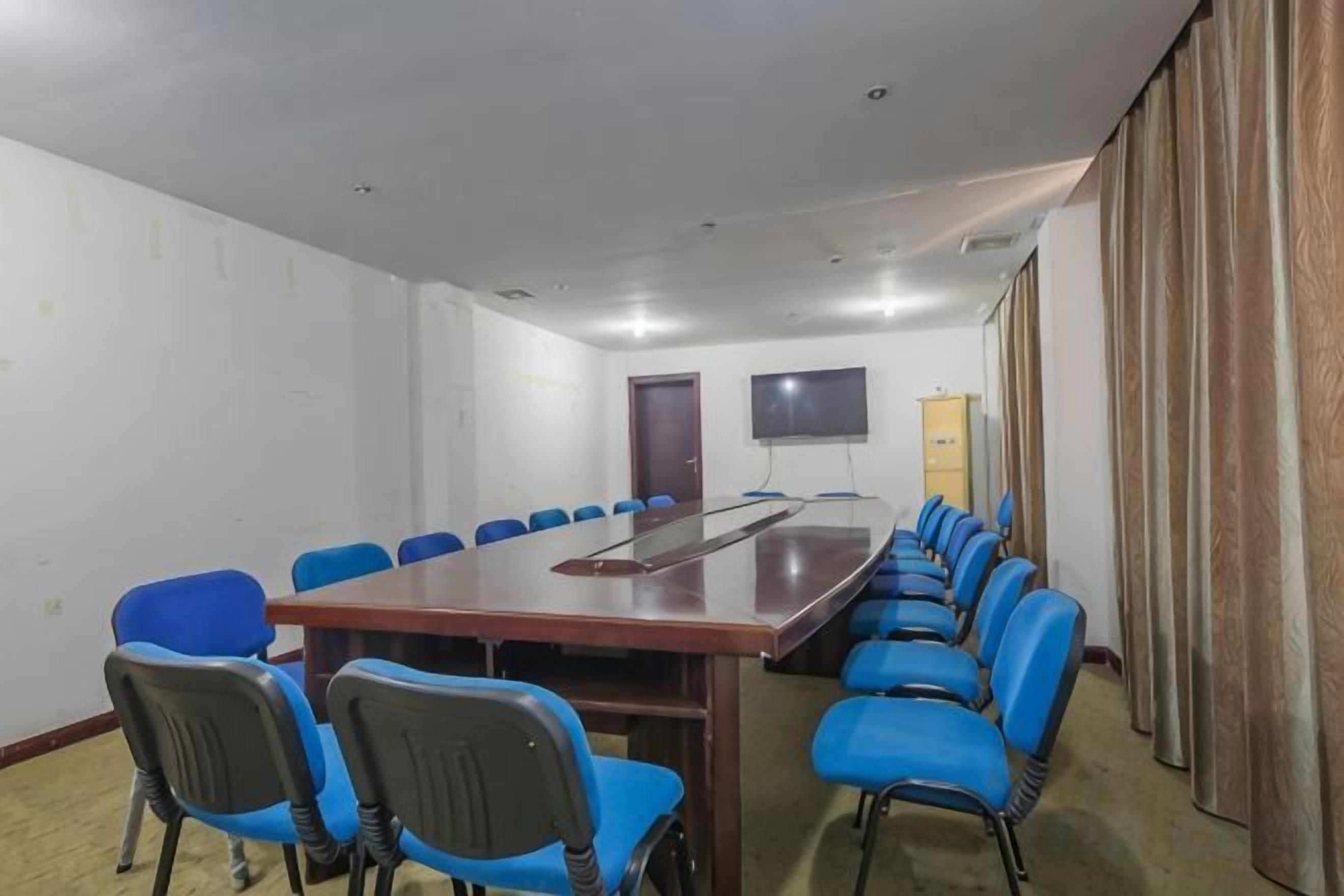 A conference room with a long table, blue chairs, a projector screen, and a door.