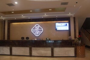 A reception desk with a digital display, a marble counter, and a wall-mounted logo.
