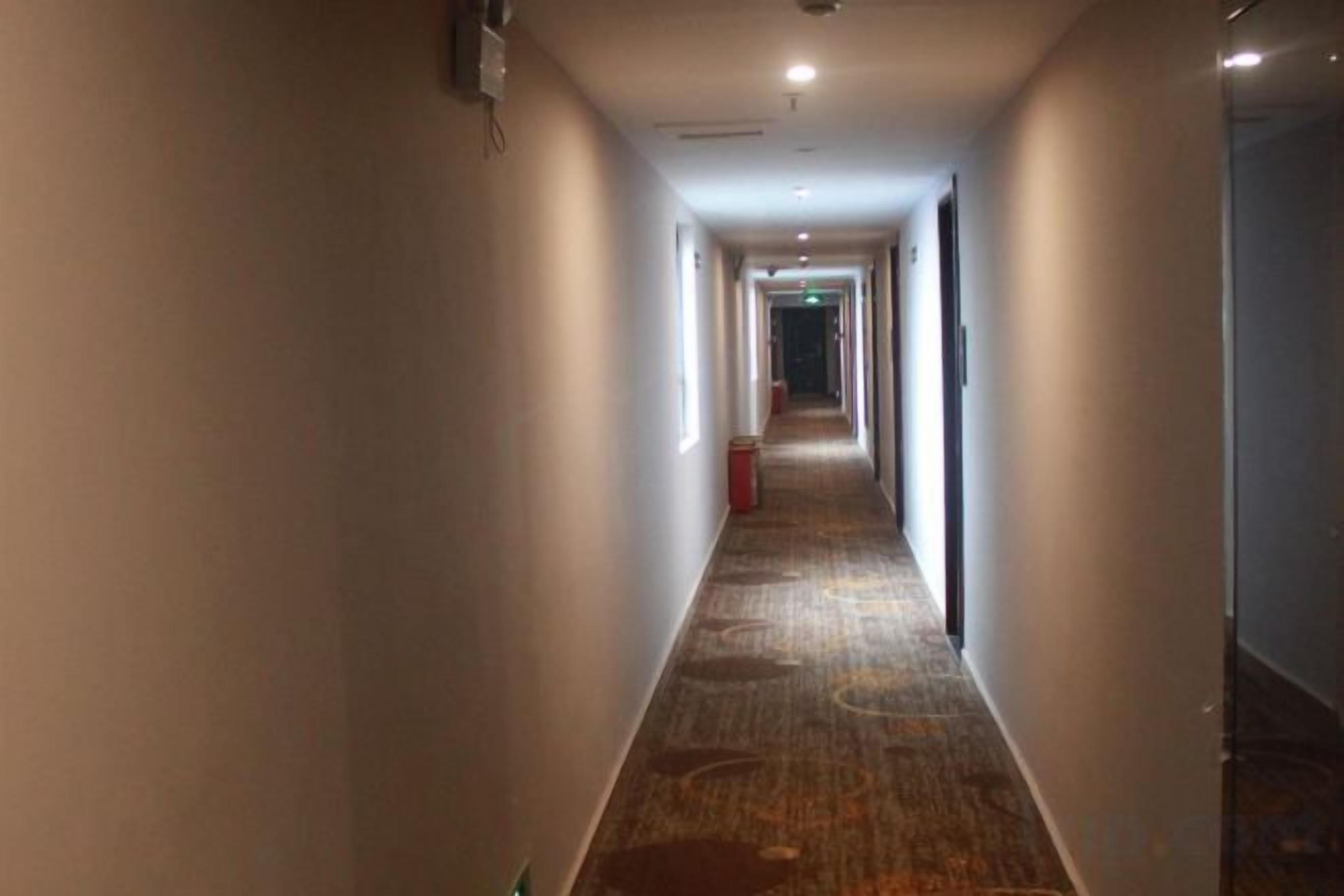 A long, narrow hotel corridor with carpeted flooring and doors on both sides.