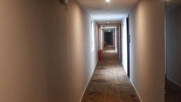 A long, narrow hotel corridor with carpeted flooring and doors on both sides.